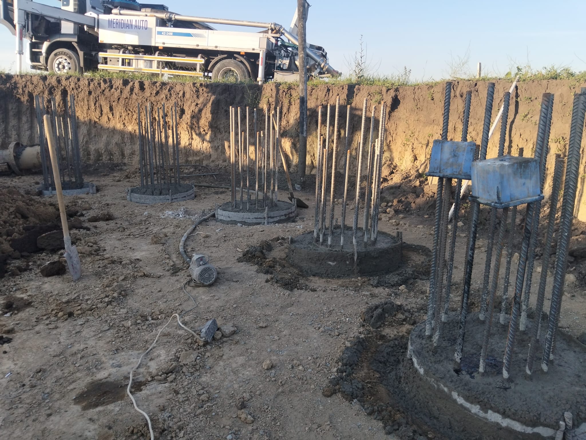 Betonarea piloților în excavație, cu echipamentul de pompare la marginea șantierului.